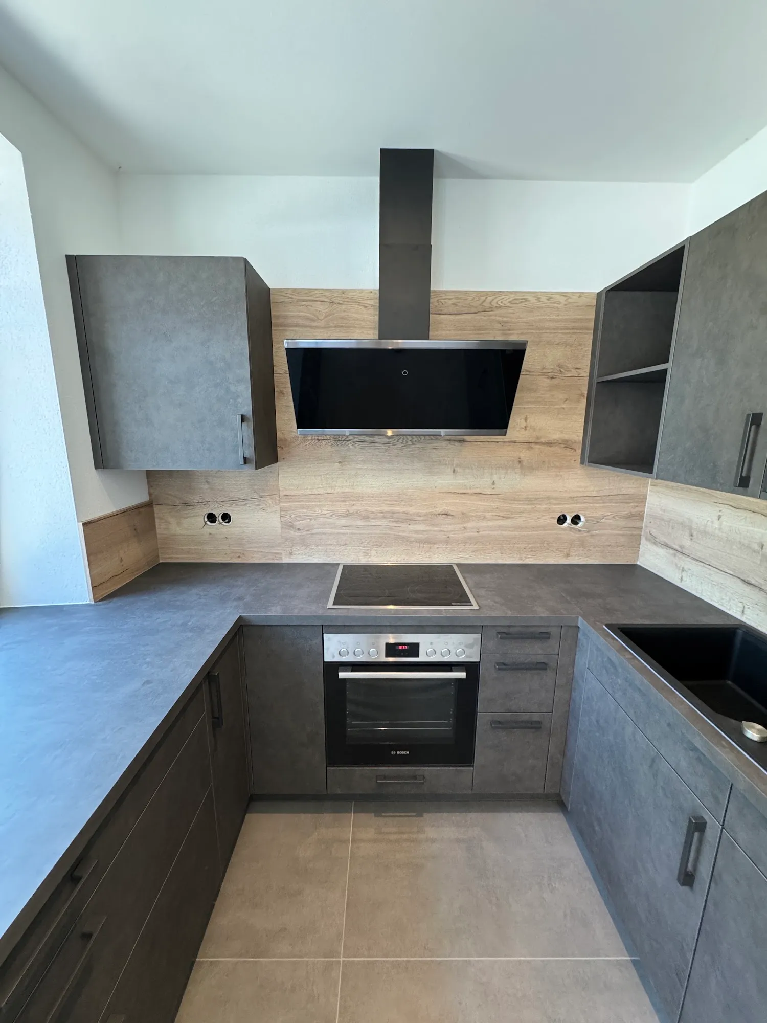 U-förmige Küche in dunklem Beton-Finish mit Holz-Rückwand und Schräghaube