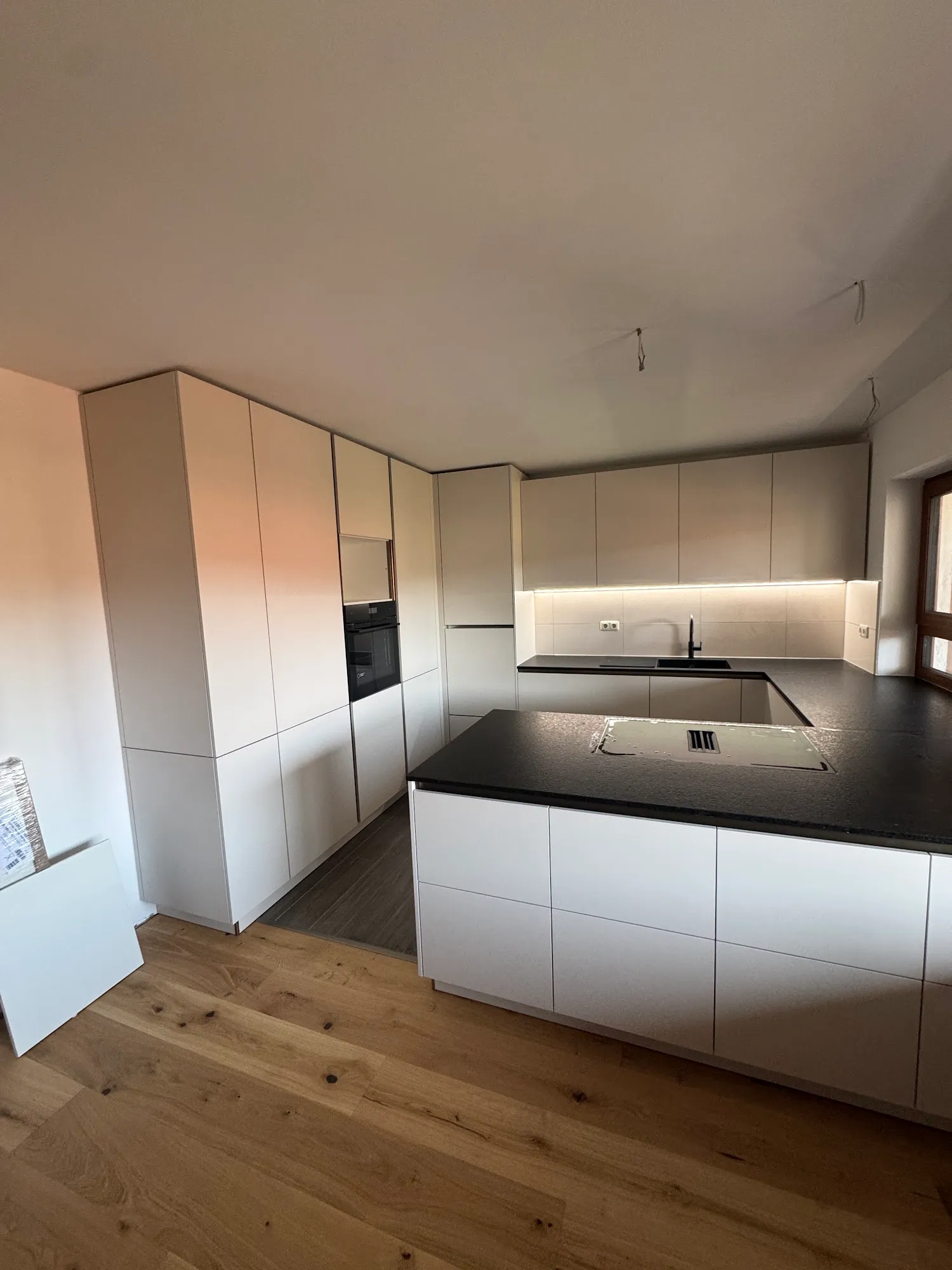 Grifflose weiße Küche mit Unterbau-LED-Beleuchtung und schwarzer Steinplatte