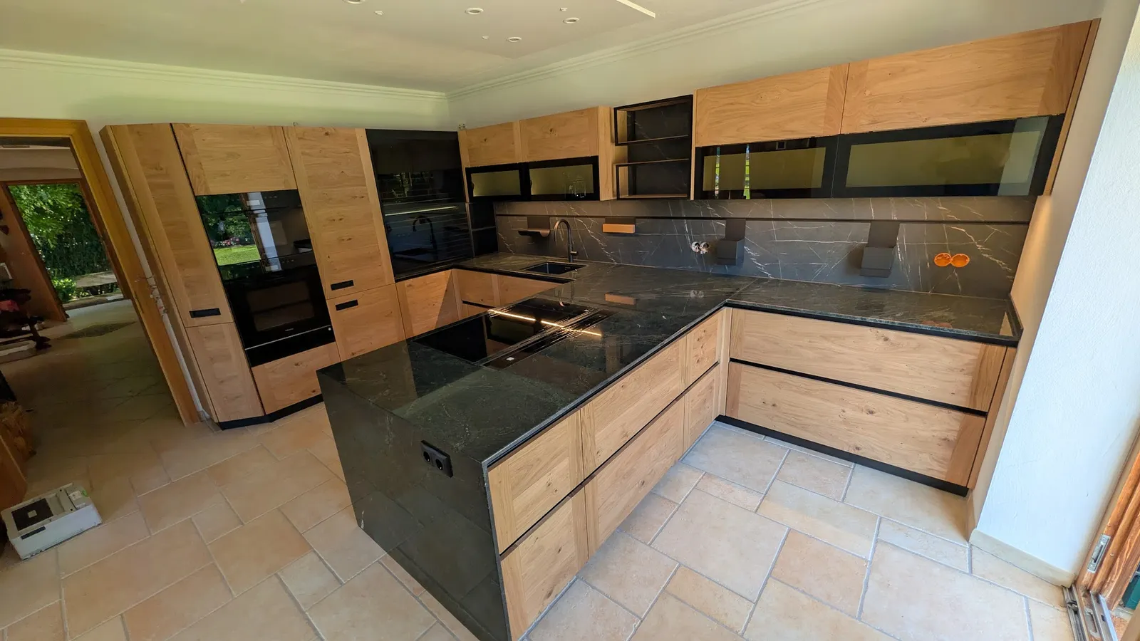 Offene Designerküche mit warmen Eichenfronten, Rauchglas-Oberschränken und Naturstein-Arbeitsplatte